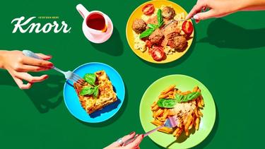 Masadaki tabaklara çatalla uzanan üç elin kuşbakışı görüntüsü.